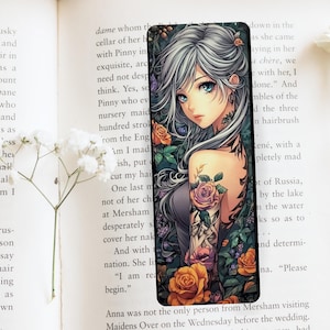 May include: A bookmark featuring a detailed illustration of a woman with long silver hair and a floral tattoo on her arm. The woman is wearing a black dress and is surrounded by flowers and greenery. The bookmark is printed on a black background.