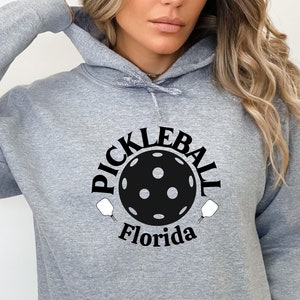 May include: A gray hoodie with a black and white graphic of a pickleball paddle and ball with the text "Pickleball Florida".