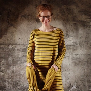 May include: A woman wearing a yellow and black striped long-sleeved shirt with a boat neck.