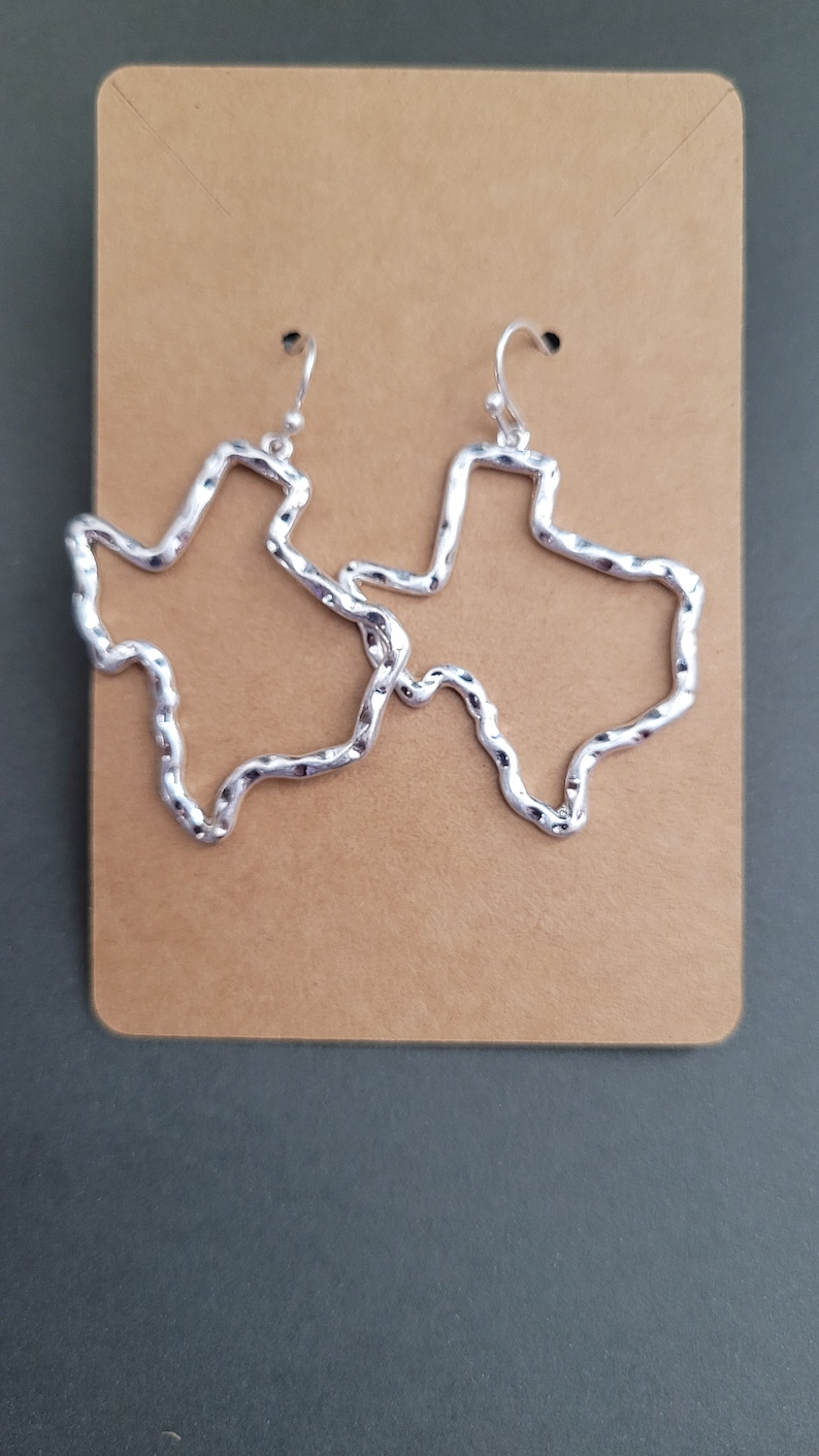 May include: A pair of silver earrings shaped like the outline of the state of Texas. The earrings are made of twisted wire and have a textured finish.