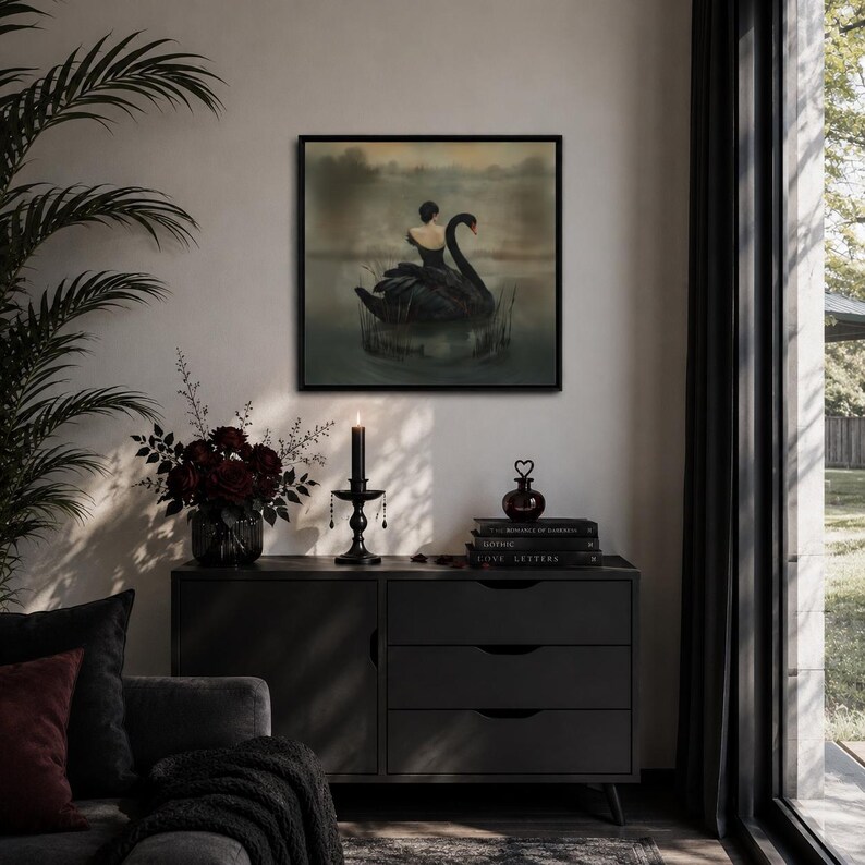 May include: A framed artwork depicts a woman on a black swan in a lake. The artwork is displayed above a dark gray cabinet with three drawers. A black candle holder, a vase of dark red roses, and decorative items are on the cabinet.