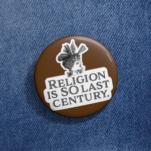 Puede incluir: Un botón marrón con un borde blanco y una ilustración en blanco y negro de una mujer con sombrero. El texto en el botón dice "Religion is so last century."