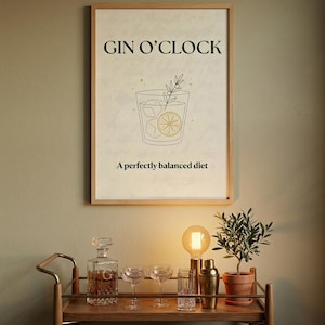 May include: A framed wall art print featuring the text GIN O'CLOCK at the top and A perfectly balanced diet at the bottom. The center illustration shows a line-art cocktail glass with ice cubes, a lemon slice, and a sprig of greenery.