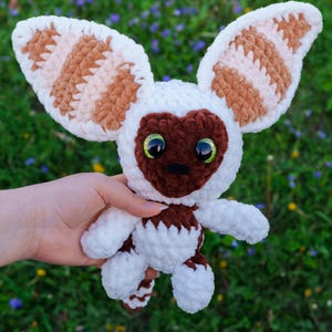 May include: A handmade crochet plush toy of a Momo character from Avatar: The Last Airbender. The plush features large, striped ears, a brown face, and green eyes. The body is white with brown accents.