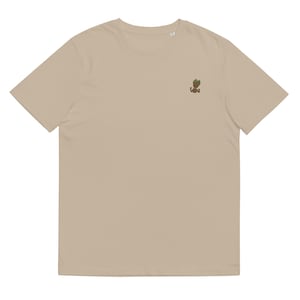 May include: A beige t-shirt with a small embroidered image of a green-haired, brown-skinned character with arms raised.