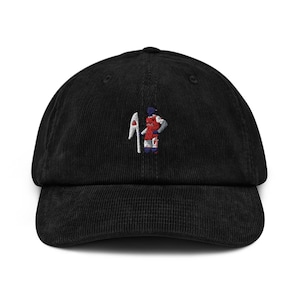 May include: Black corduroy baseball cap with an embroidered design of a person holding a flag.