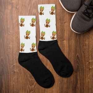 May include: A pair of white socks with a black and white pattern of a cartoon character with green hair and brown skin. The character is flexing its muscles. The socks are black at the ankle and toe.