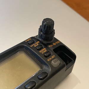 May include: Black handheld radio with a black knob on top. The radio has a small LCD screen and several buttons labeled "PWR", "VFO/MR", "SKIP", "HOME", "DTMF", "VOL/SQL", "SCH.SET", and "SCH".