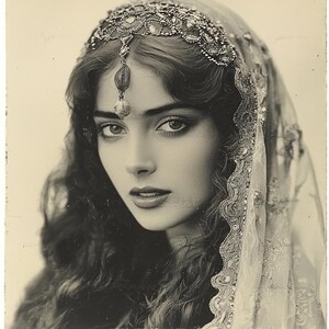 May include: A black and white portrait of a woman wearing a beaded headpiece and a sheer veil. The woman has long, dark hair and is looking directly at the camera.