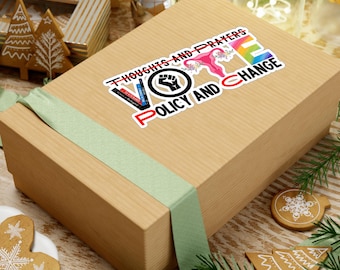Può includere: Una scatola regalo marrone con un nastro verde. La scatola ha un adesivo che dice "Thoughts and Prayers Vote Policy and Change". L'adesivo presenta un pugno, un utero e un arcobaleno.