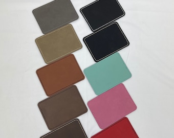 May include: Ten leather coasters in various colors, including gray, beige, brown, black, teal, pink, and red. Each coaster has a stitched edge.