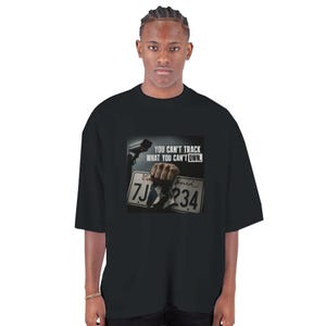 Puede incluir: Una camiseta negra de manga corta con un estampado gráfico de una mano sosteniendo una matrícula de California con el texto "YOU CAN'T TRACK WHAT YOU CAN'T OWN." y una cámara de seguridad visible en la esquina superior izquierda del diseño.