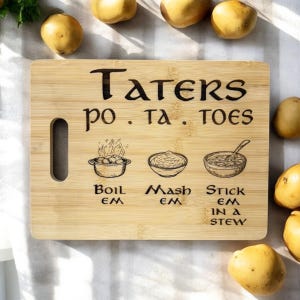 May include: A wooden chopping board with the text "Taters po. ta. toes" and illustrations of potato dishes. The board has a handle and the text "Boil em, Mash em, Stick em in a stew". Potatoes are scattered around the board.