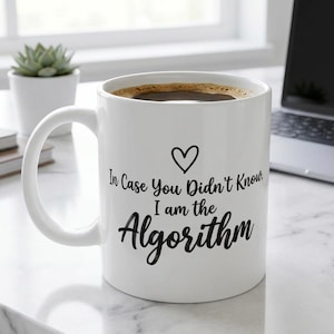 May include: A white ceramic mug featuring a black heart icon and the printed text "In Case You Didn't Know, I am the Algorithm" in a combination of serif and script fonts. The mug is filled with dark coffee and has a curved handle on the left side.