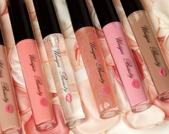 May include: Seven tubes of lip gloss with black caps and labels that say "Unique Beauty" with a pink lip print. The tubes are arranged in a row on a background of white and pink rose petals.