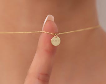 May include: A delicate gold chain necklace featuring a small, round, flat pendant. The pendant is engraved with the date 21.06.18. The necklace is suspended by a thin gold chain that rests against the skin, showcasing the circular charm.
