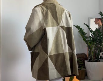 Könnte beinhalten: Eine Jacke mit geometrischem Muster in Olivgrün-, Beige- und Brauntönen. Die Jacke hat einen Kragen und eine lockere Passform. Die Person trägt eine weiße Hose und beige Stiefel. Das Design der Jacke besteht aus einer Reihe von Dreiecken.
