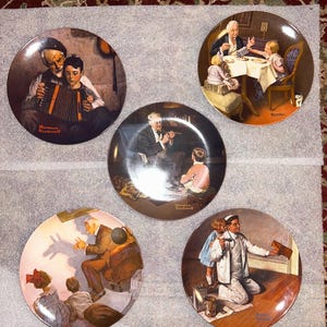 Puede incluir: Cinco platos decorativos con ilustraciones de Norman Rockwell. Cada plato representa una escena diferente con personas, mostrando diversas actividades. Los platos tienen un acabado brillante y se exhiben sobre una superficie neutra.