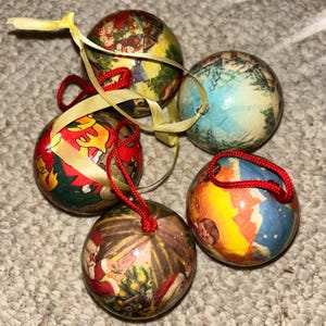 May include: Five round Christmas baubles with vintage illustrations. Each bauble has a different design, with red, yellow, and blue colours. Some have red string loops and yellow ribbon for hanging on the tree.