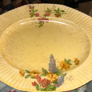 May include: Oval yellow serving platter with a floral design. The platter has a ribbed edge and is decorated with colourful flowers in shades of red, yellow, and blue. The flowers are arranged in clusters around the edges.