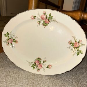 Puede incluir: Plato ovalado para servir de color crema con borde festoneado y ribete plateado. El plato está decorado con racimos de rosas rosas y hojas verdes. Una pieza vintage para servir comida.