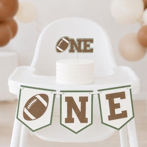 以下が含まれることがあります： 白いハイチェア。ケーキトッパーには「ONE」と書かれており、「O」の代わりにアメリカンフットボールのグラフィックが描かれています。トレイには、アメリカンフットボールと「N」「E」の文字が茶色と白でデザインされた3枚のペナントが吊り下げられています。