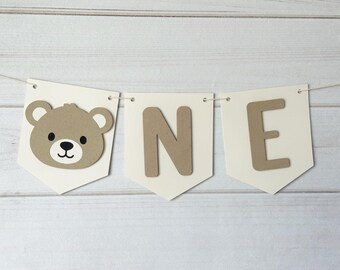 May include: White banner with brown felt letters spelling "ONE" and a brown felt bear face.