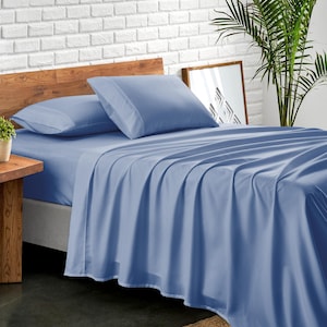 May include: A blue bed sheet with two matching pillowcases on a wooden bed frame. The bed is against a white brick wall.