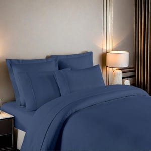 May include: A blue duvet cover with four matching pillowcases. The bedding is made of a soft, smooth fabric and has a simple, elegant design.