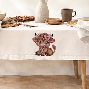 May include: Embroidered image of a Highland cow calf with a pink bow. The calf is brown with pink accents on its ears and hooves. The image is on a white tablecloth, with a neutral background.