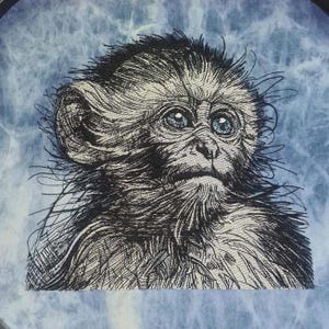 Puede incluir: Un dibujo en blanco y negro de un mono con ojos azules. El mono mira hacia la derecha y tiene una expresión seria. El fondo es un patrón de tie-dye azul y blanco.