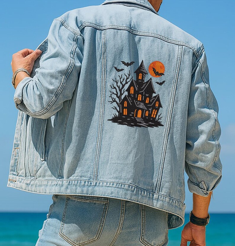 May include: Light blue denim jacket featuring a Halloween-themed graphic on the back. The graphic includes a haunted house, bats, and a full orange moon. The jacket has a classic design with button closures and pockets.