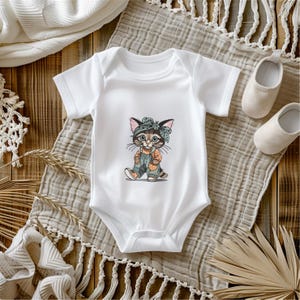 Puede incluir: Body de beb&eacute; blanco con un dise&ntilde;o de gato de dibujos animados. El gato lleva una diadema, un peto y zapatos en tonos marr&oacute;n, naranja y azul. El body se muestra sobre una superficie neutra, con zapatos de beb&eacute;.
