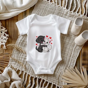 May include: White baby onesie featuring a black dog and a white cat hugging, surrounded by red hearts. The onesie is short-sleeved and has a snap closure. The design is an embroidered graphic. The background includes baby shoes and a neutral-colored blanket.
