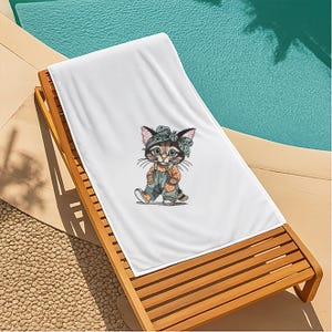 Puede incluir: Toalla de playa blanca con una ilustraci&oacute;n de dibujos animados de un gato con peto y diadema. El gato es marr&oacute;n, gris y naranja. La toalla est&aacute; sobre una tumbona de madera junto a una piscina.