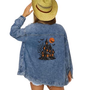 May include: A light blue denim jacket with a Halloween-themed graphic on the back. The graphic features a haunted house, bats, and a full orange moon. The jacket has a classic button-up design.
