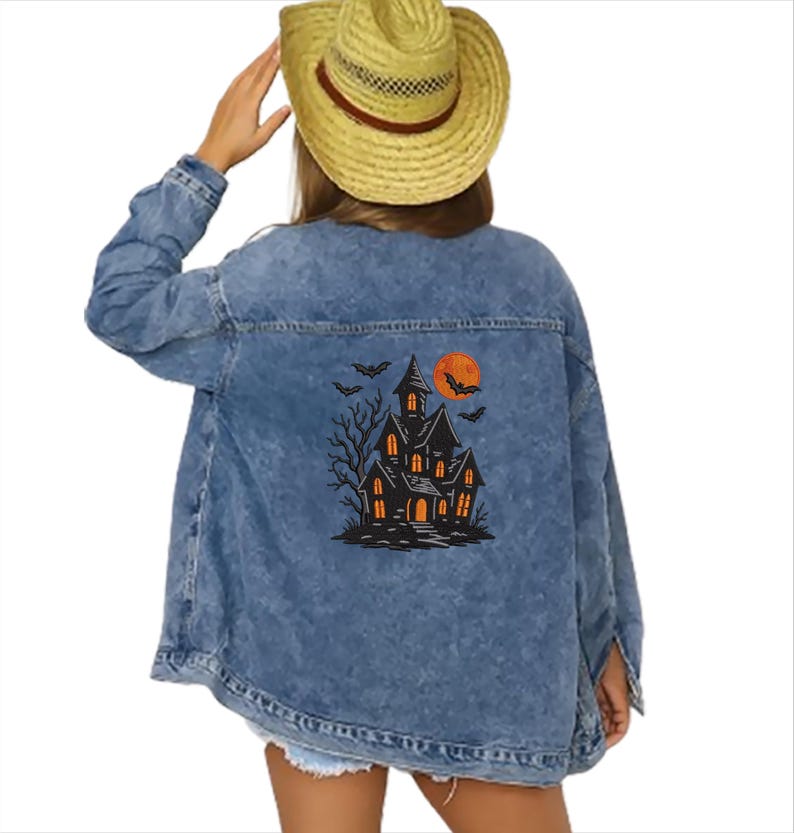 May include: A light blue denim jacket with a Halloween-themed graphic on the back. The graphic features a haunted house, bats, and a full orange moon. The jacket has a classic button-up design.