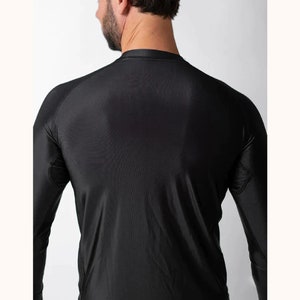 May include: A black long-sleeve compression shirt featuring a crew neckline and raglan sleeves. The garment is constructed from a smooth, synthetic fabric with visible stitching details along the shoulder seams and underarm panels.