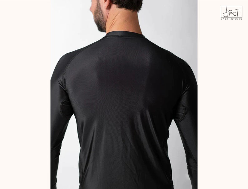 May include: A black long-sleeve compression shirt featuring a crew neckline and raglan sleeves. The garment is constructed from a smooth, synthetic fabric with visible stitching details along the shoulder seams and underarm panels.