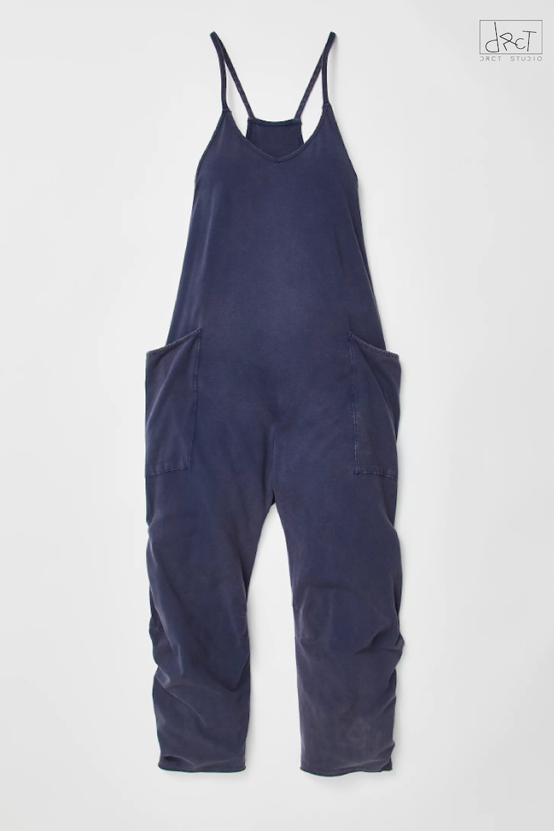 May include: A dark blue sleeveless jumpsuit with two large pockets on the front. The jumpsuit has a V-neck and thin straps.