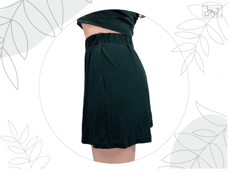 May include: A dark green skirt with an elasticized waistband and a simple, straight-cut silhouette. The garment is shown from a side profile view, featuring a smooth, solid-colored fabric that falls to a hemline above the knee.