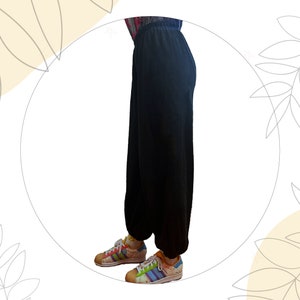 Pu&ograve; includere: Pantaloni neri a tinta unita dal taglio ampio con vita elasticizzata e polsini arricciati alle caviglie. I pantaloni sono abbinati a scarpe da ginnastica basse con un motivo a righe multicolore, lacci bianchi e punta in gomma testurizzata.
