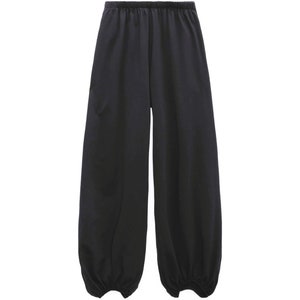 Pu&ograve; includere: Pantaloni neri a tinta unita caratterizzati da una silhouette ampia e rilassata, con vita elasticizzata e polsini arricciati alle caviglie. Il capo &egrave; realizzato in un tessuto liscio e opaco che cade morbidamente lungo le gambe.