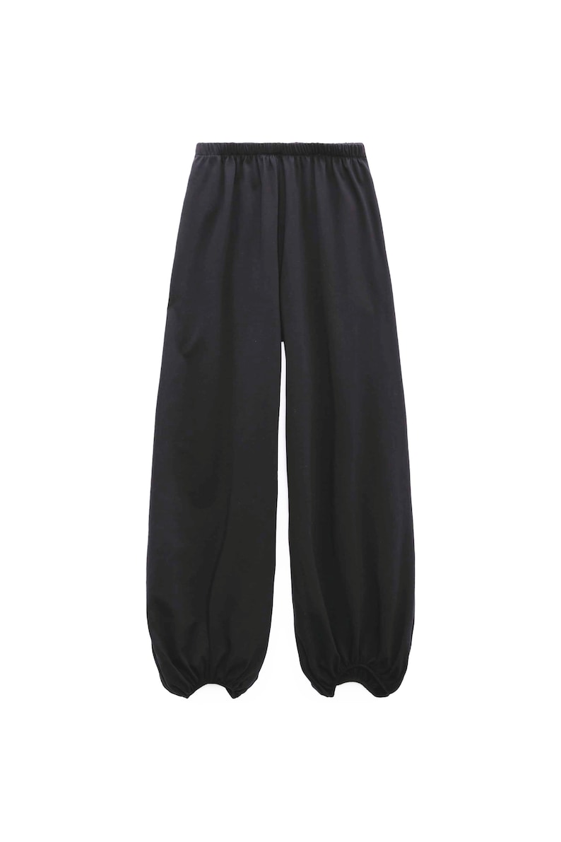 Pu&ograve; includere: Pantaloni neri a tinta unita caratterizzati da una silhouette ampia e rilassata, con vita elasticizzata e polsini arricciati alle caviglie. Il capo &egrave; realizzato in un tessuto liscio e opaco che cade morbidamente lungo le gambe.