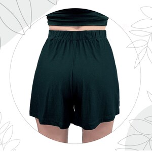 May include: Dark forest green shorts featuring a high-waisted design with an elasticized waistband. The shorts have a relaxed, loose-fitting leg silhouette and a smooth, solid-colored fabric construction, captured from a rear-facing perspective.