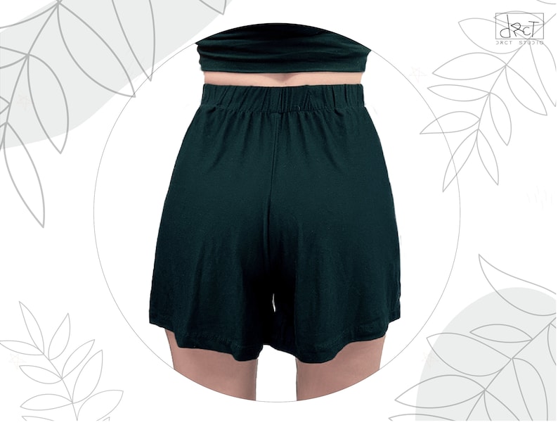 May include: Dark forest green shorts featuring a high-waisted design with an elasticized waistband. The shorts have a relaxed, loose-fitting leg silhouette and a smooth, solid-colored fabric construction, captured from a rear-facing perspective.