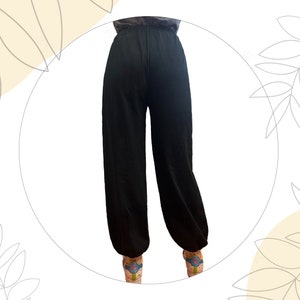 Pu&ograve; includere: Pantaloni neri a tinta unita con vita alta, elastico in vita e una silhouette a gamba larga e rilassata che si restringe leggermente alle caviglie. I pantaloni sono mostrati di schiena, evidenziando una struttura semplice e priva di decorazioni.