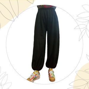 Pu&ograve; includere: Pantaloni neri a tinta unita dal taglio ampio, dotati di vita elasticizzata e polsini elastici alle caviglie. I pantaloni sono indossati con scarpe da ginnastica multicolore a fantasia con lacci bianchi e calzini gialli con una piccola icona smiley.