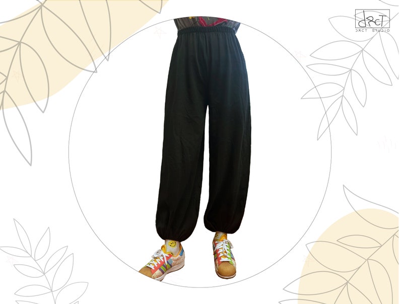 Pu&ograve; includere: Pantaloni neri a tinta unita dal taglio ampio, dotati di vita elasticizzata e polsini elastici alle caviglie. I pantaloni sono indossati con scarpe da ginnastica multicolore a fantasia con lacci bianchi e calzini gialli con una piccola icona smiley.