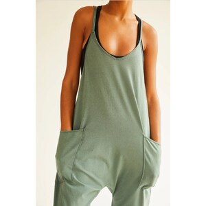 May include: A sage green jumpsuit with a scoop neck and two large pockets on the front. The jumpsuit is made of a soft, comfortable fabric.